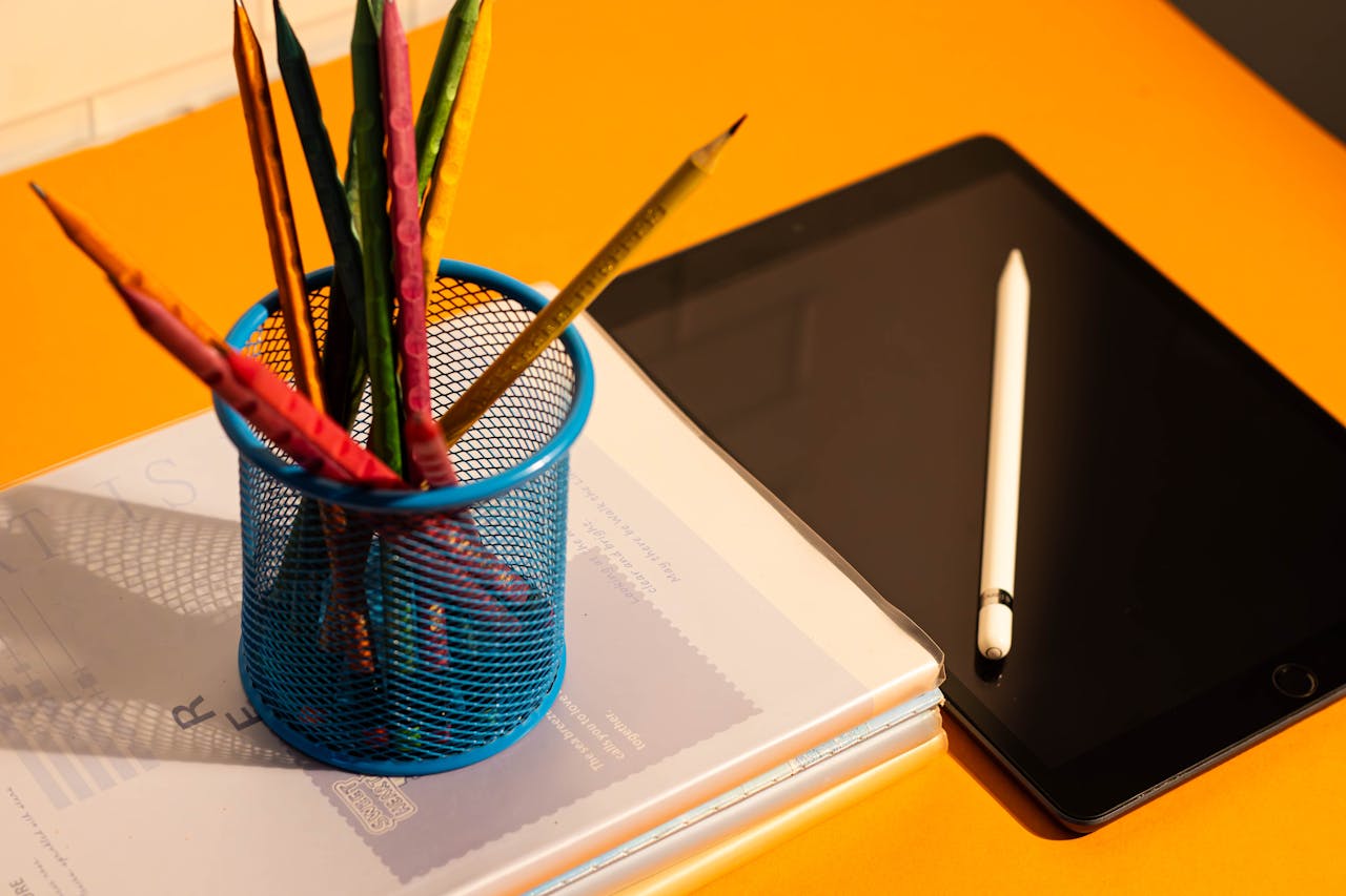 Bright flat lay of pencils and tablet on an orange desk, perfect for school or office scenes.