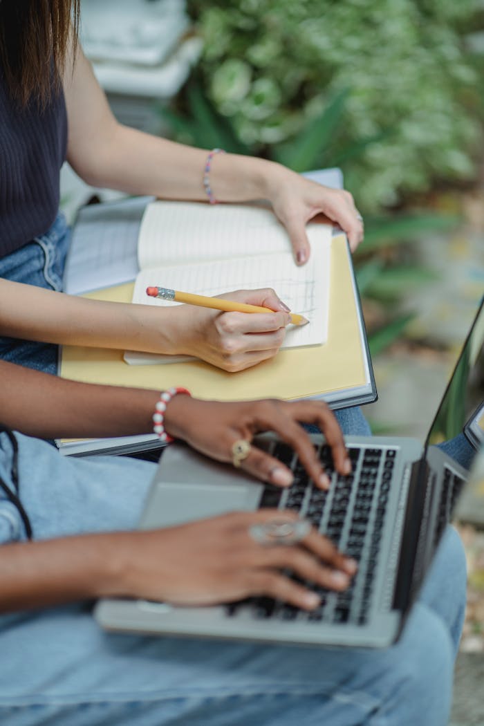 Two women studying outdoors with a laptop and notebook, embodying teamwork.