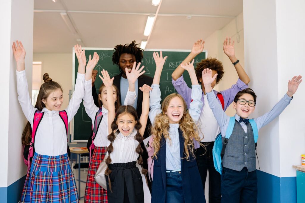 Joyful group of diverse school children raising their hands in an indoor classroom setting.